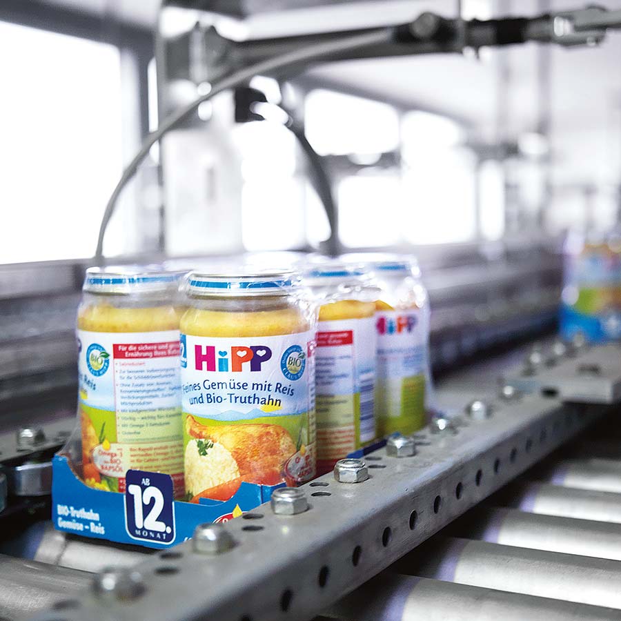 Jars of baby food are moving on a conveyor belt in a factory setting.