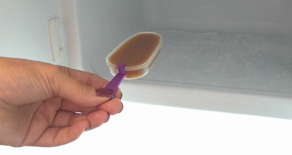 Blakus ledusskapja atvilktnei ar ledus pildītu atvilktni kāda roka tur popsi ar violetu rokturi.